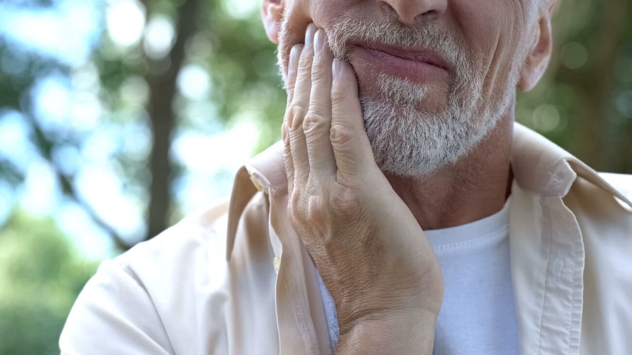 older man holding his jaw in pain tmj pain treatment restorative dentistry dentist in Jackson Heights New York